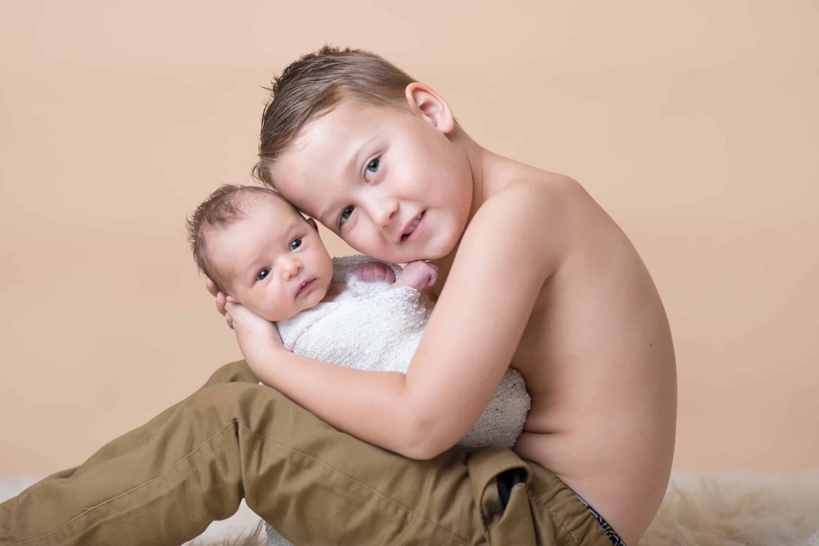 big brother holding little newborn baby sister wrapped